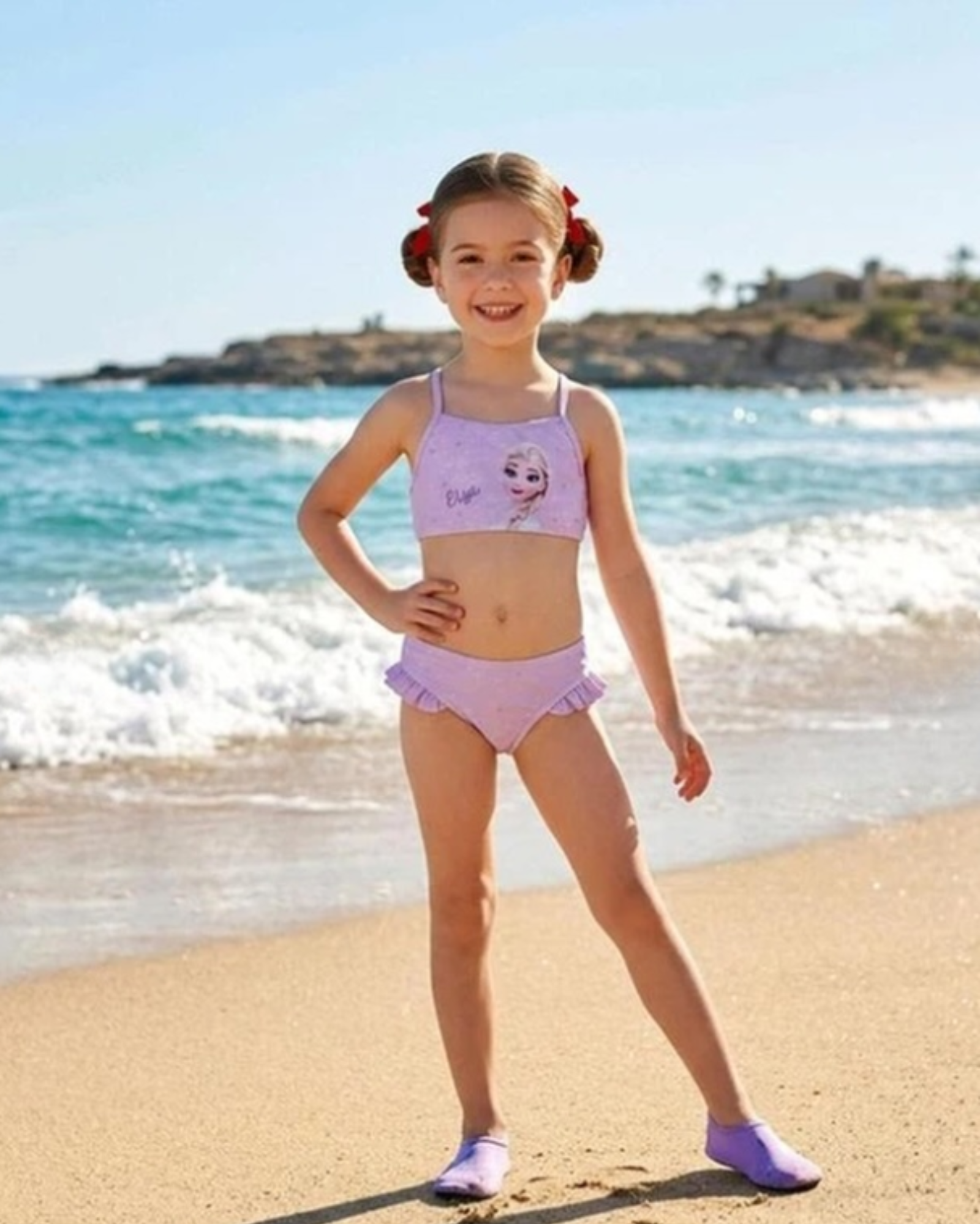 Young girl in a pink swimsuit standing on a beach with ocean waves in the background