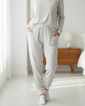 Person wearing gray pajama set in a bright room with wooden furniture.