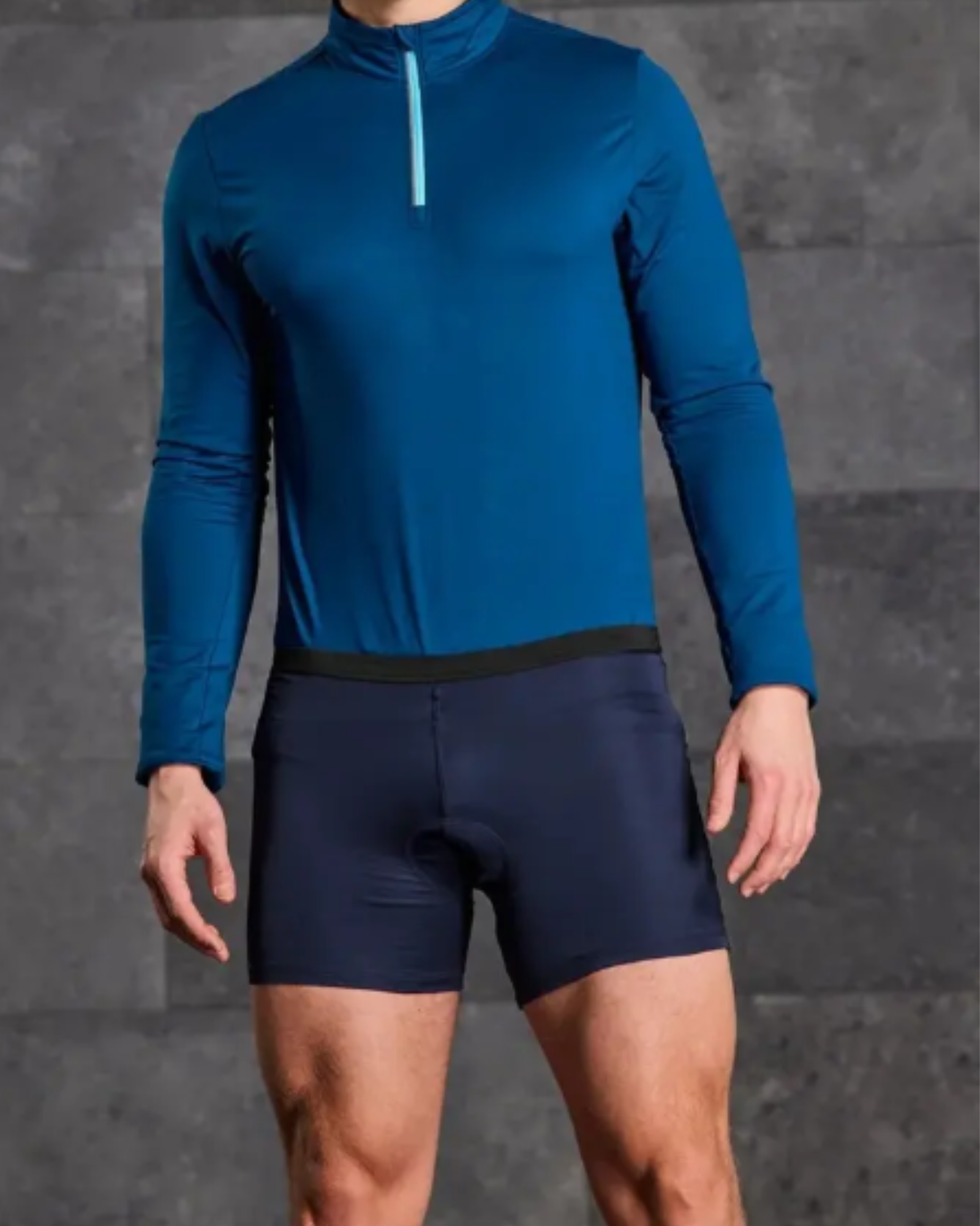 Person wearing a blue long-sleeve athletic top and navy shorts on a gray background
