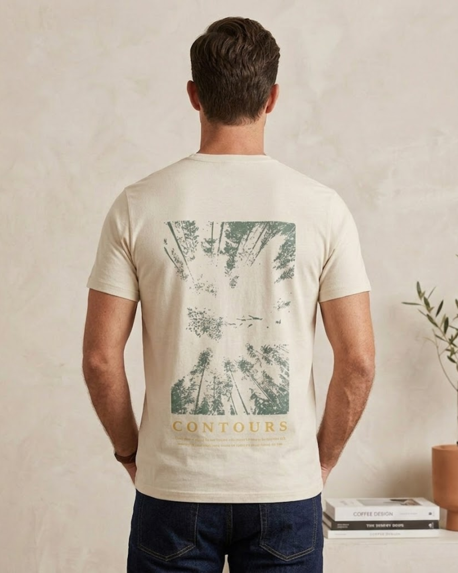Man wearing a beige t-shirt with a forest graphic and 'Contours' text on the back, standing against a neutral wall.