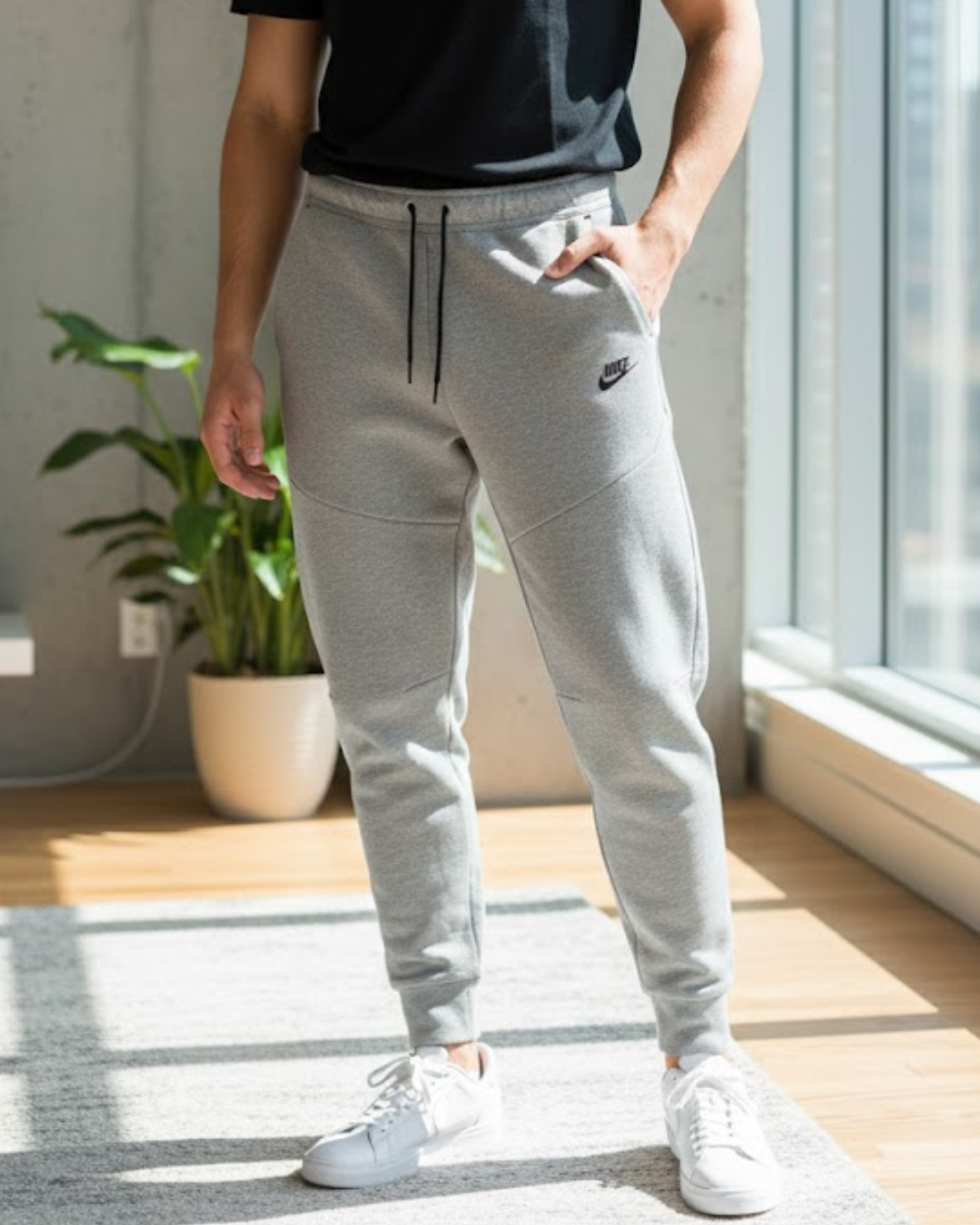 Person wearing gray Nike jogger pants in a room with a plant and window.