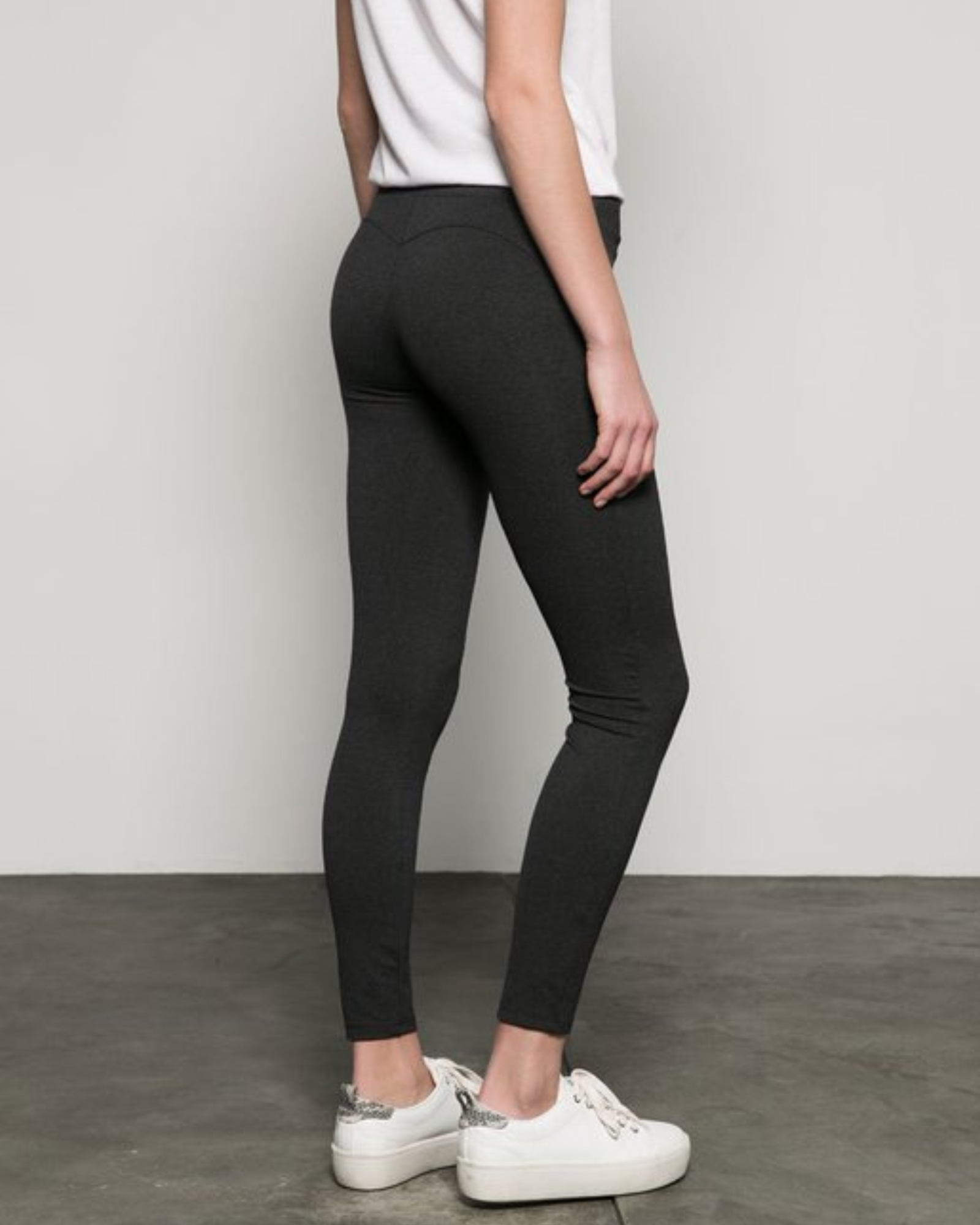 Person wearing olive green leggings and white sneakers against a plain background