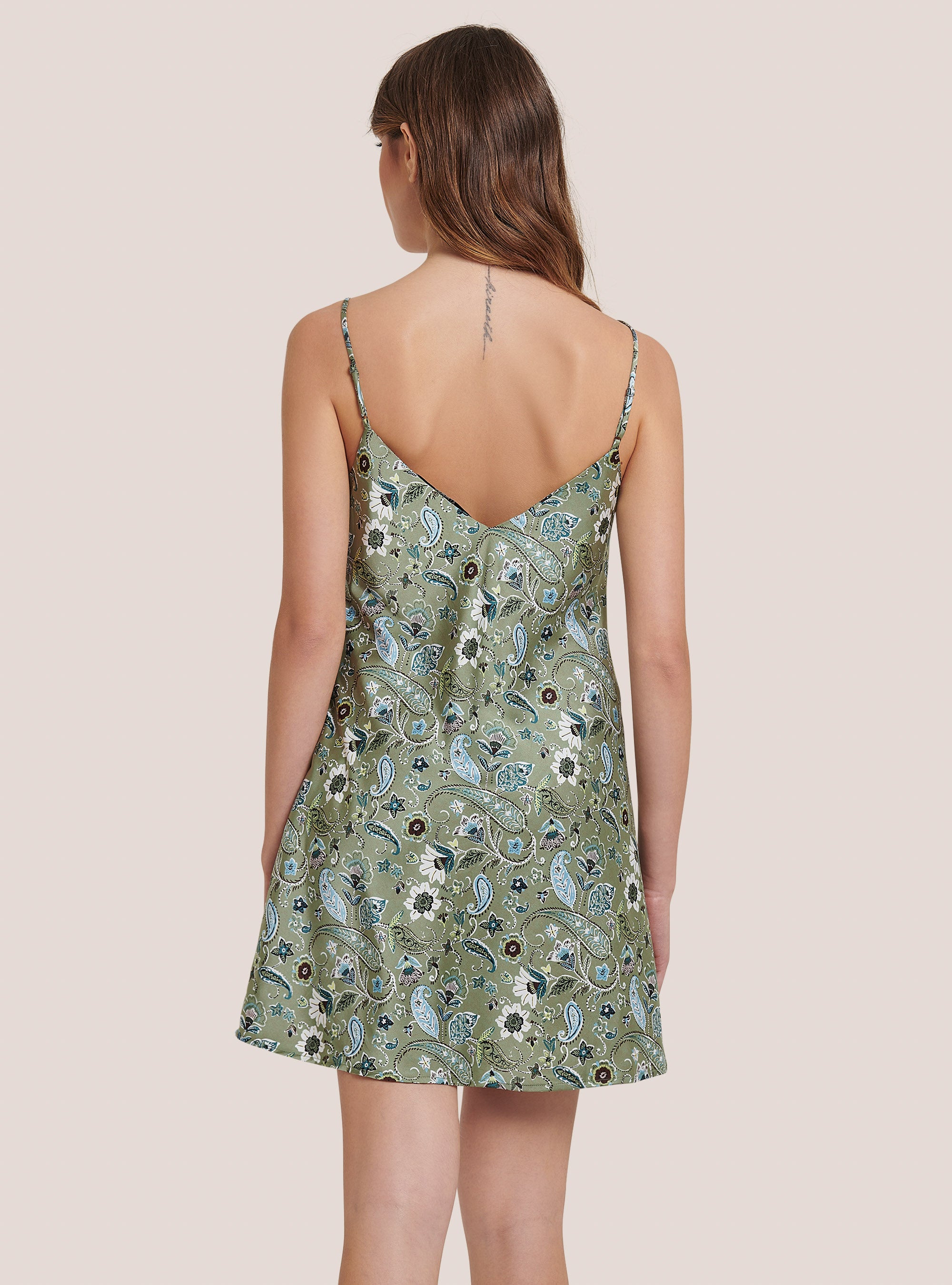 Woman wearing a green floral patterned slip dress on a beige background