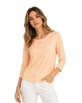 Woman wearing a peach long-sleeve top and white pants on a white background