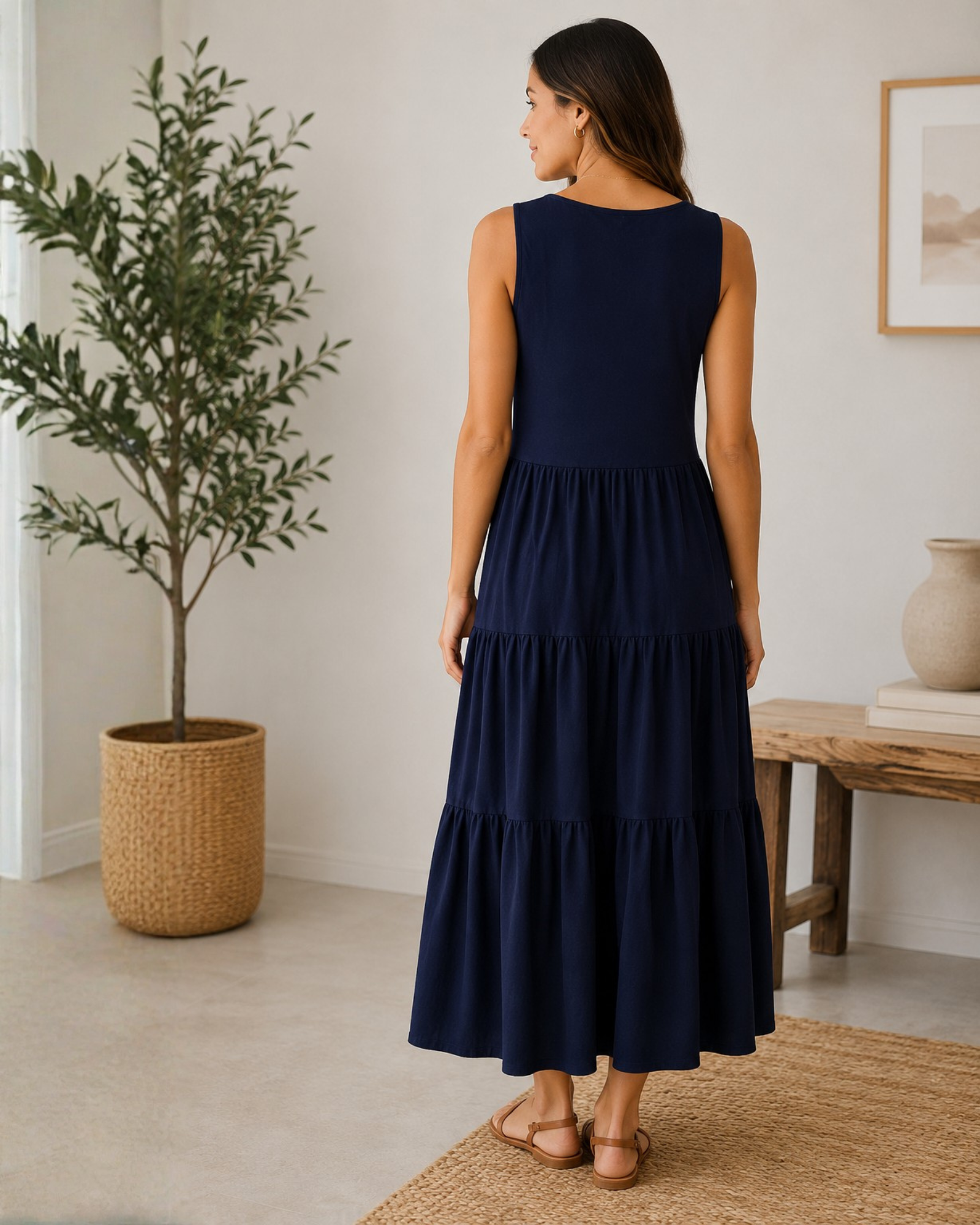 Woman wearing a navy blue dress standing in a room with a plant and a table.