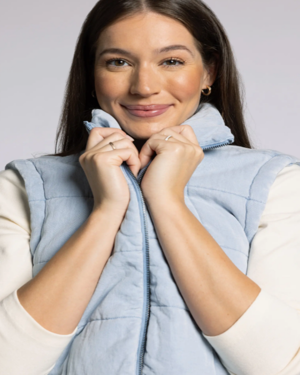 Woman wearing a light blue puffer vest against a plain background
