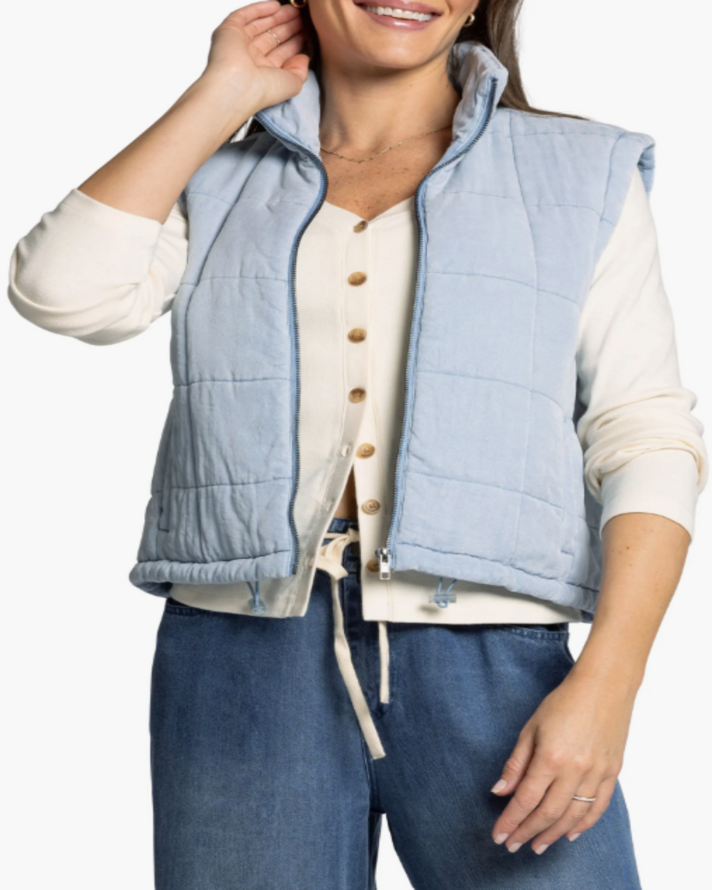 Woman wearing a light blue quilted vest over a cream shirt with a white background
