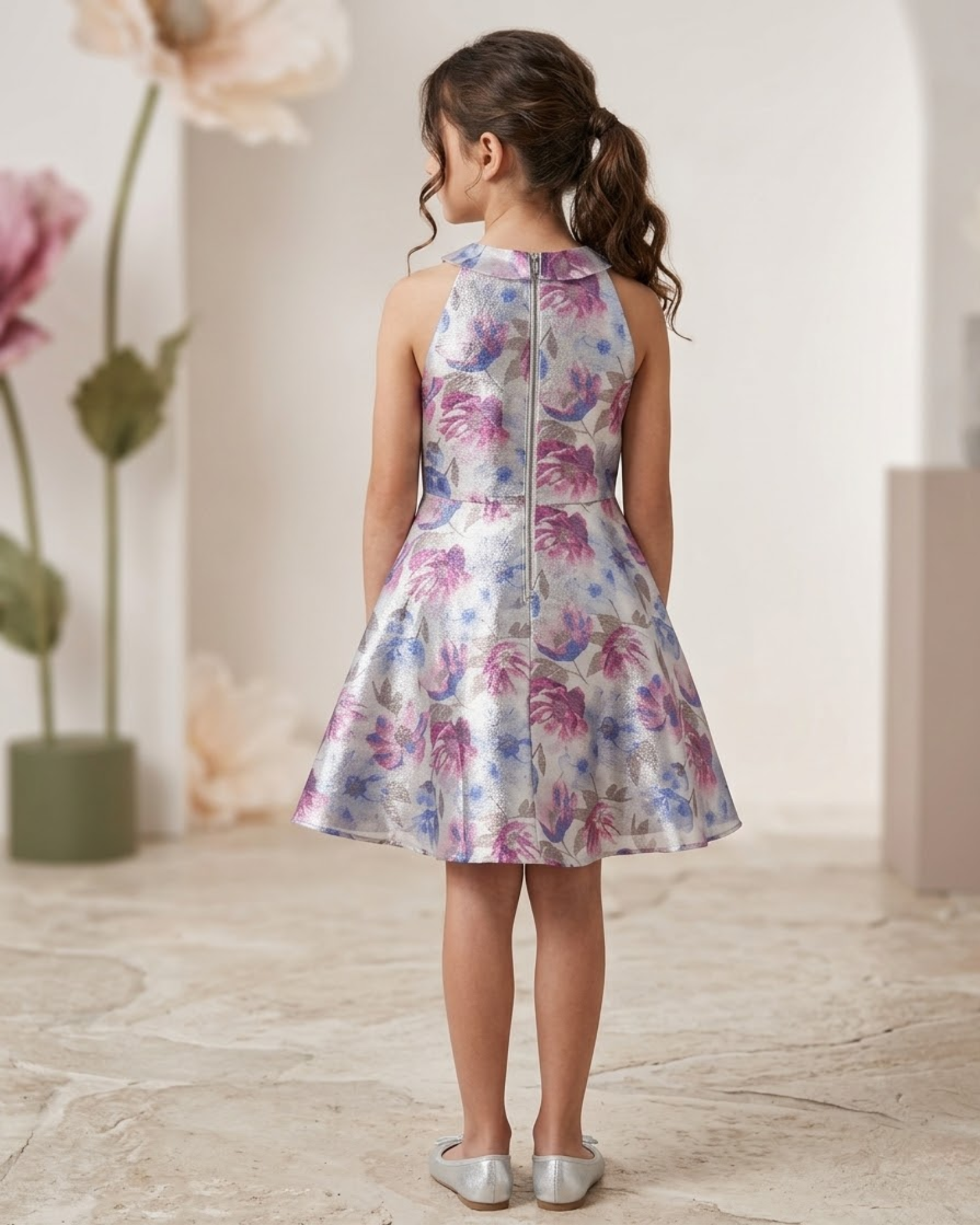 Young girl wearing a floral dress standing in a softly lit room with flowers in the background.