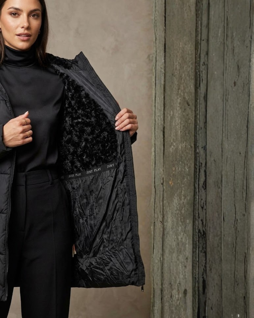 Woman holding a black jacket with a textured inner lining against a neutral background