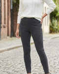 Person wearing dark gray pants and a white sweater on a cobblestone street.