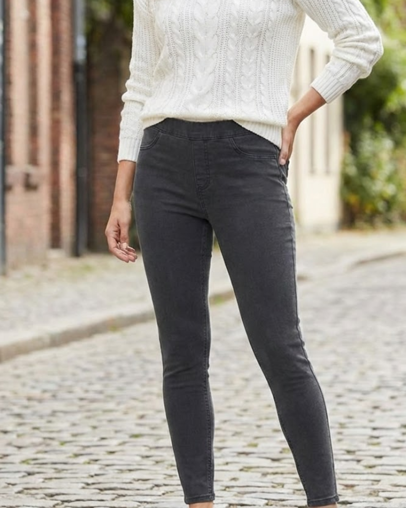 Person wearing dark gray pants and a white sweater on a cobblestone street.