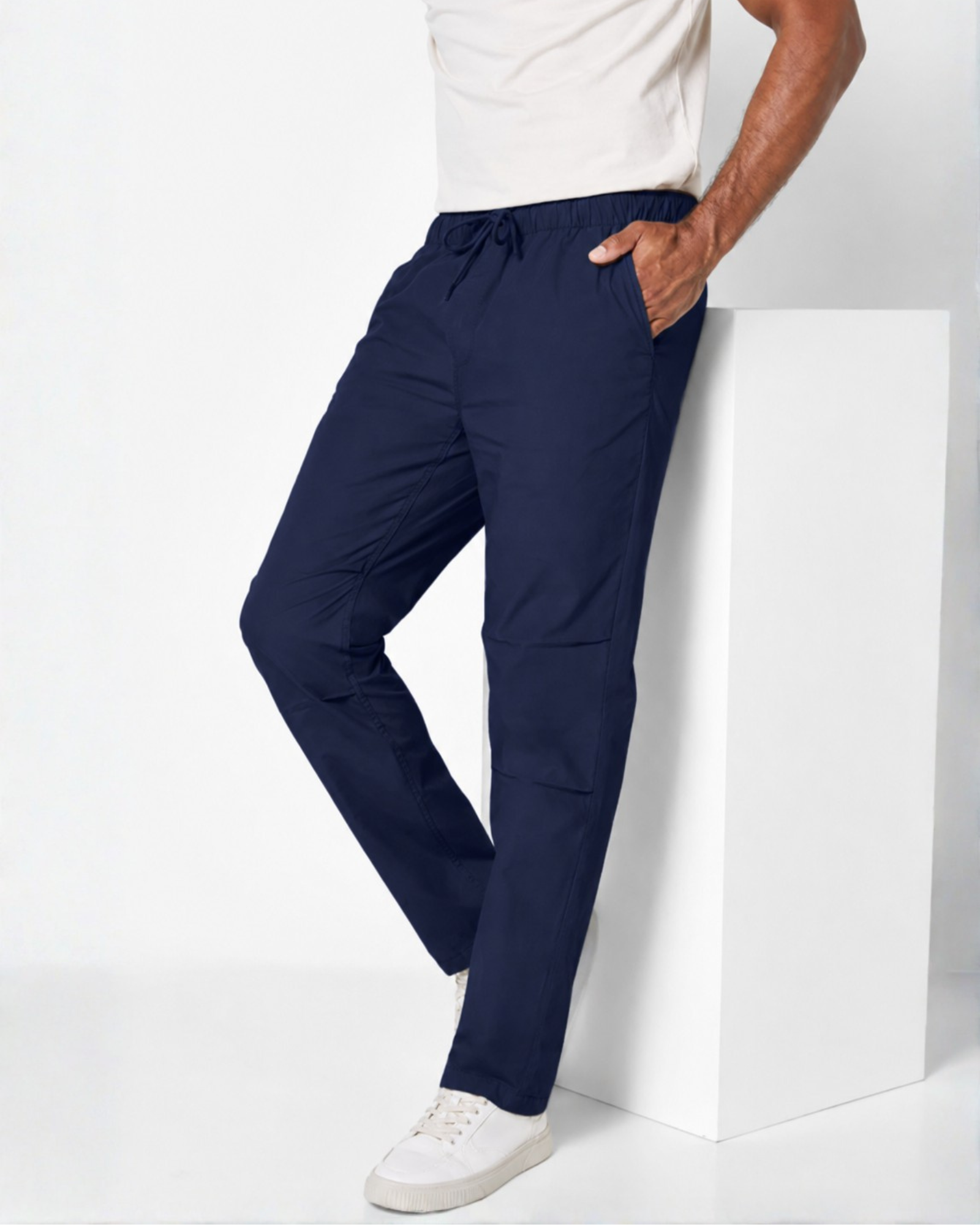 a men wearing white basic top with a sneakers footwear and a lightweight navy trouser