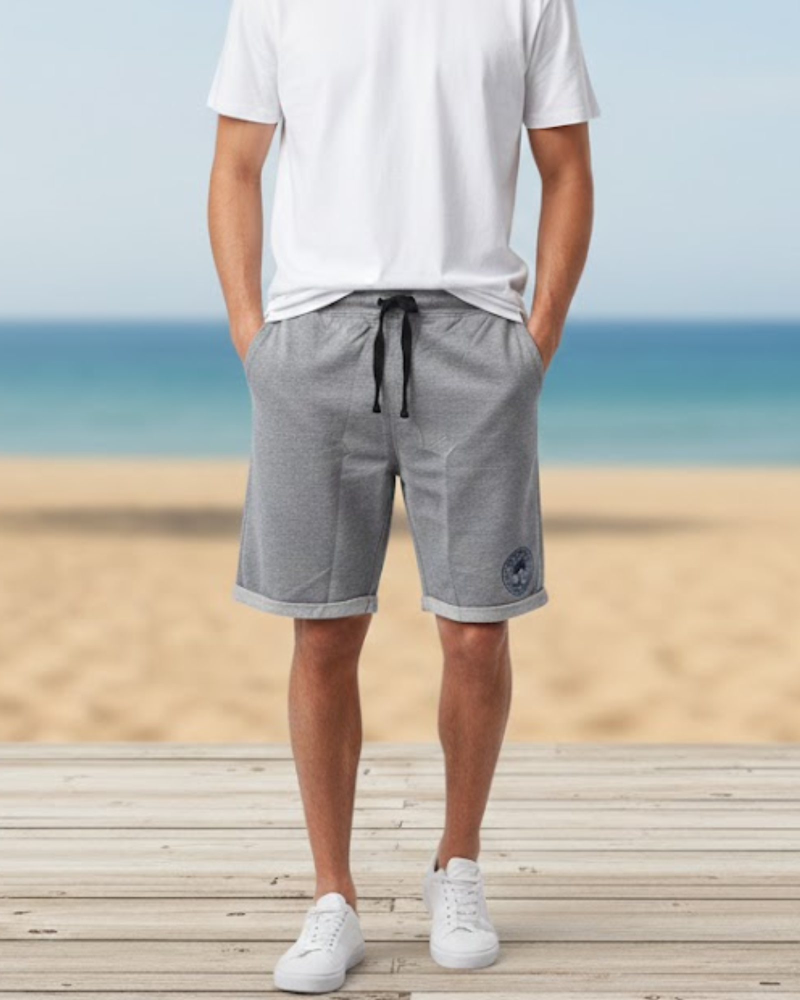 Person wearing gray shorts and white sneakers on a wooden platform with a beach background