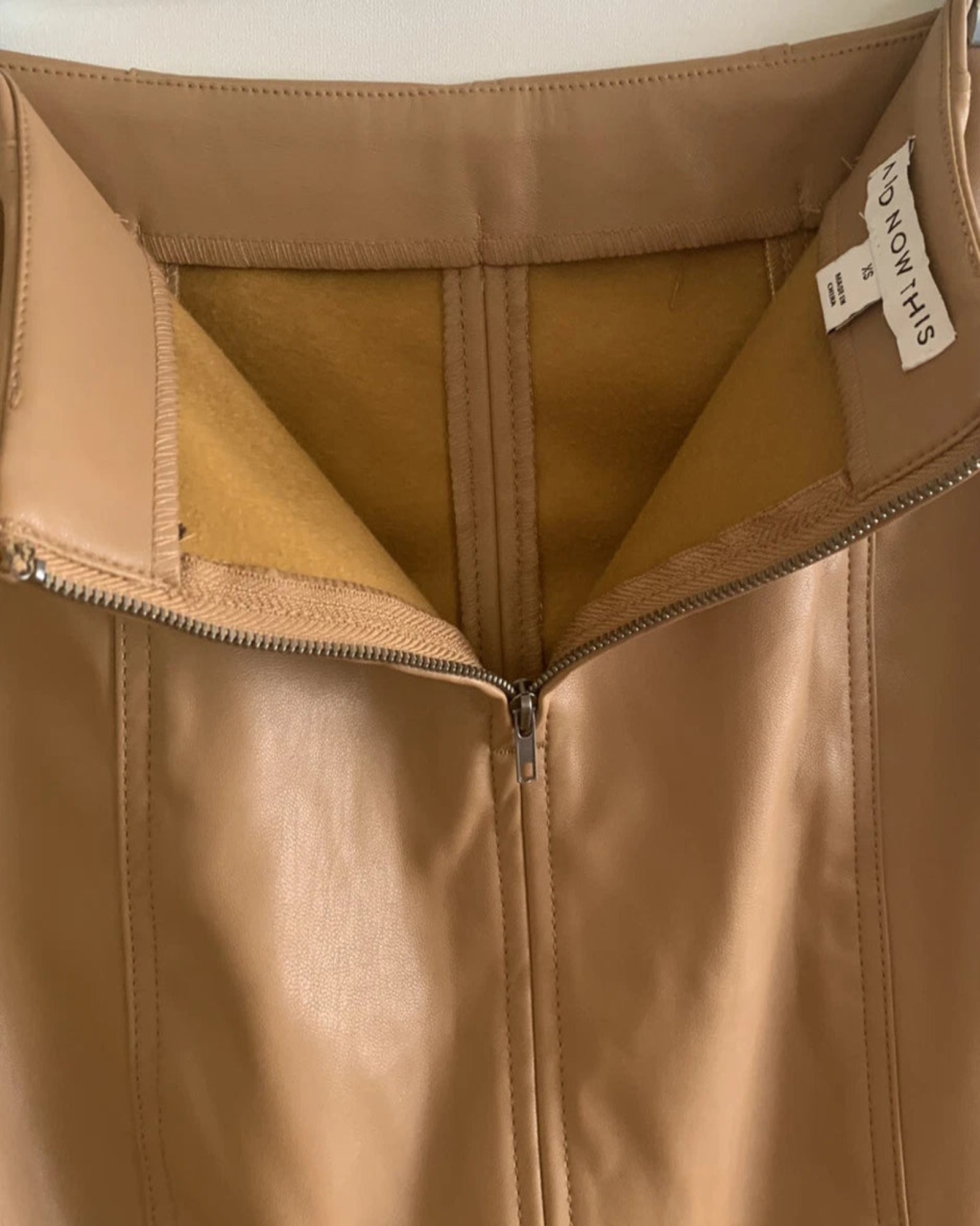Close-up of a tan leather skirt with a brand label on the interior.