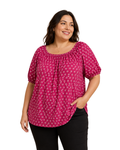 A woman modeling a bright pink short-sleeve top with a white circular pattern, paired with black pants, against a plain white background.