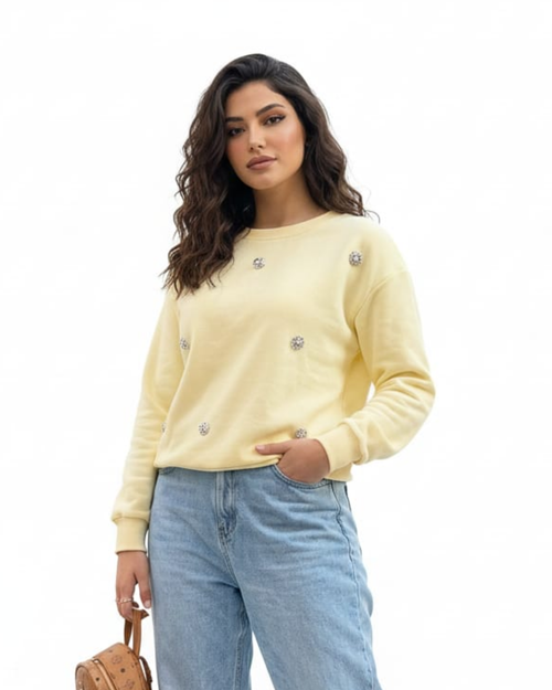 Woman wearing a light yellow sweater with decorative buttons and light blue jeans