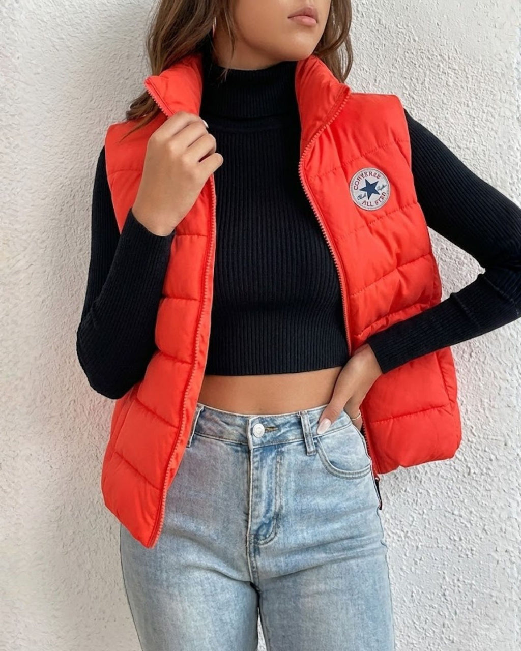 Person wearing a red puffer vest with a brand logo, black long-sleeve top, and blue jeans 