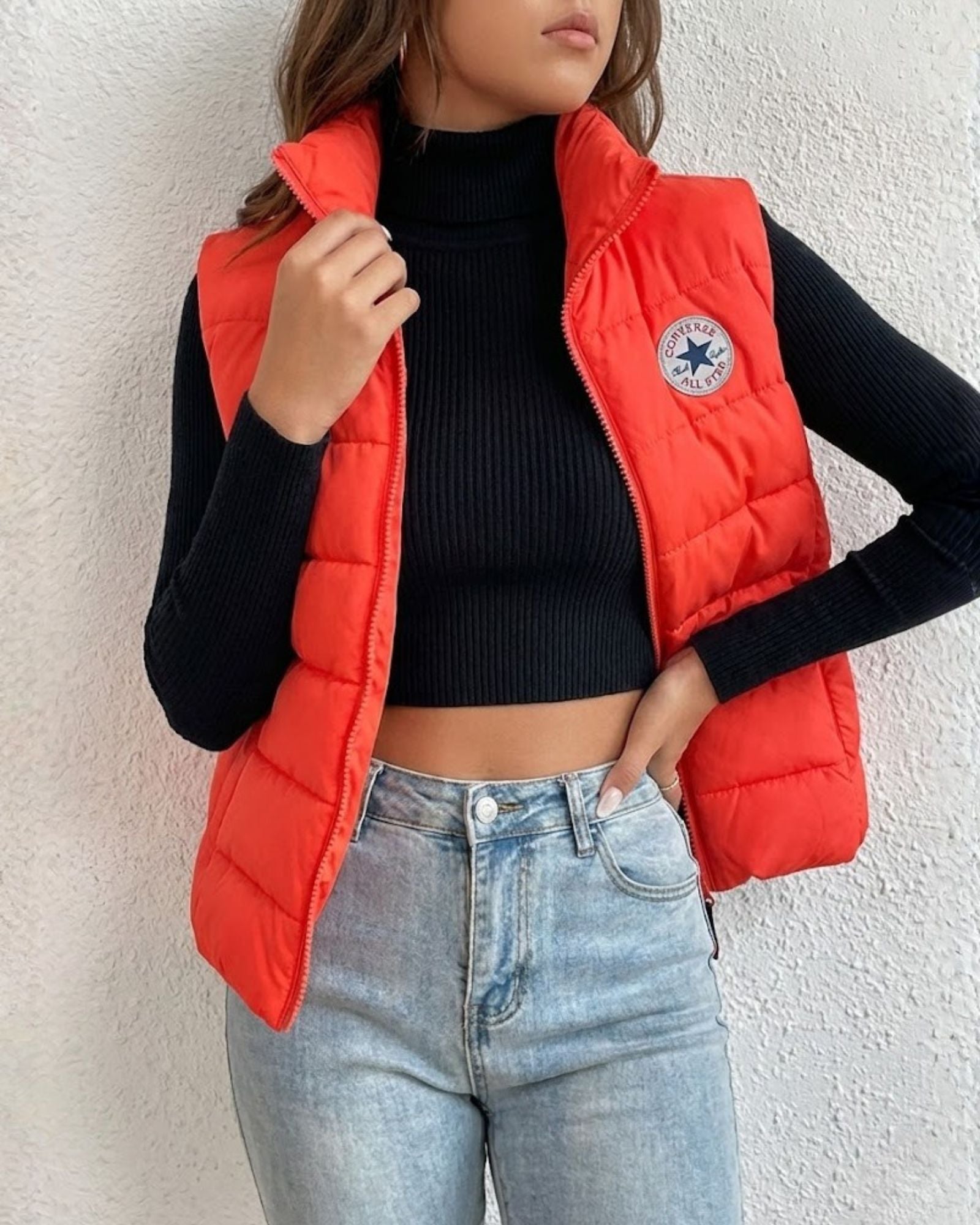 Person wearing a red puffer vest with a brand logo, black long-sleeve top, and blue jeans 