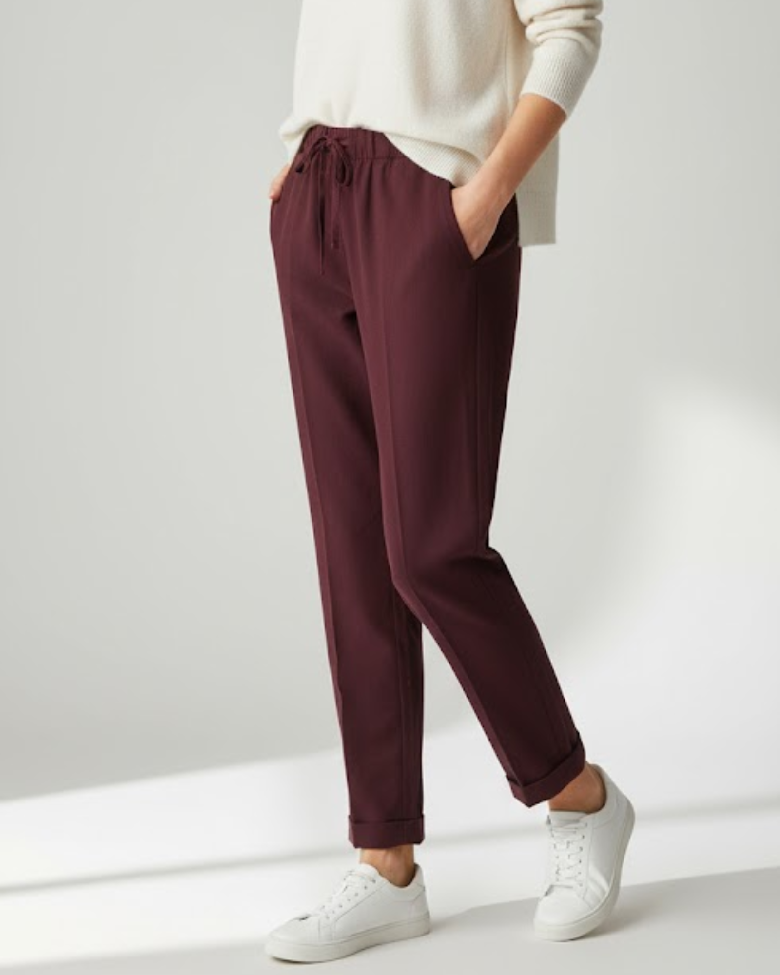 Maroon pants worn with a white sweater and white sneakers on a light gray background