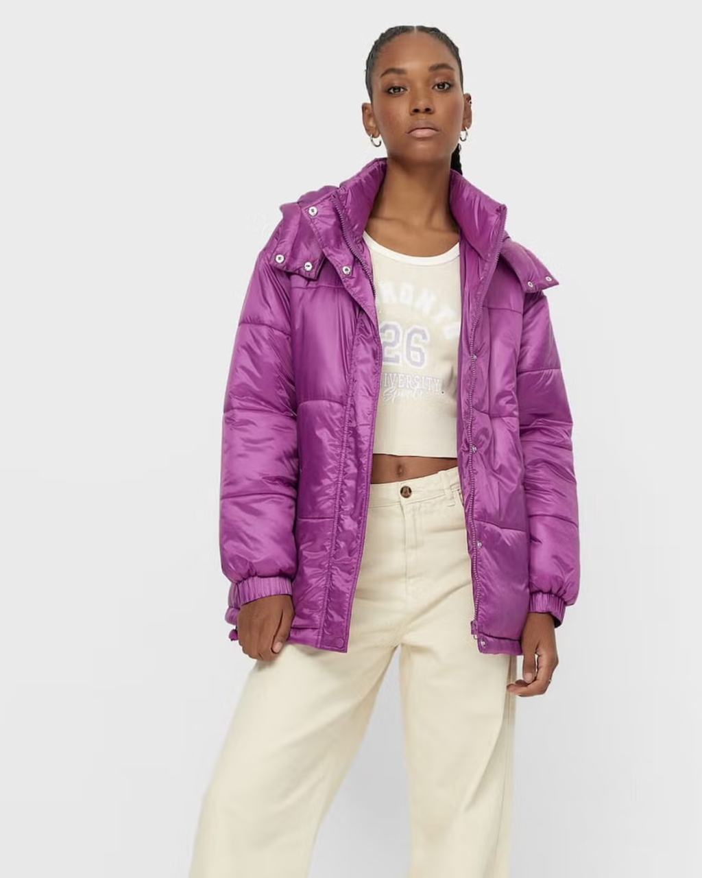 women wearing a trendy purple puffer jacket over a white top and beige pants on a light gray background