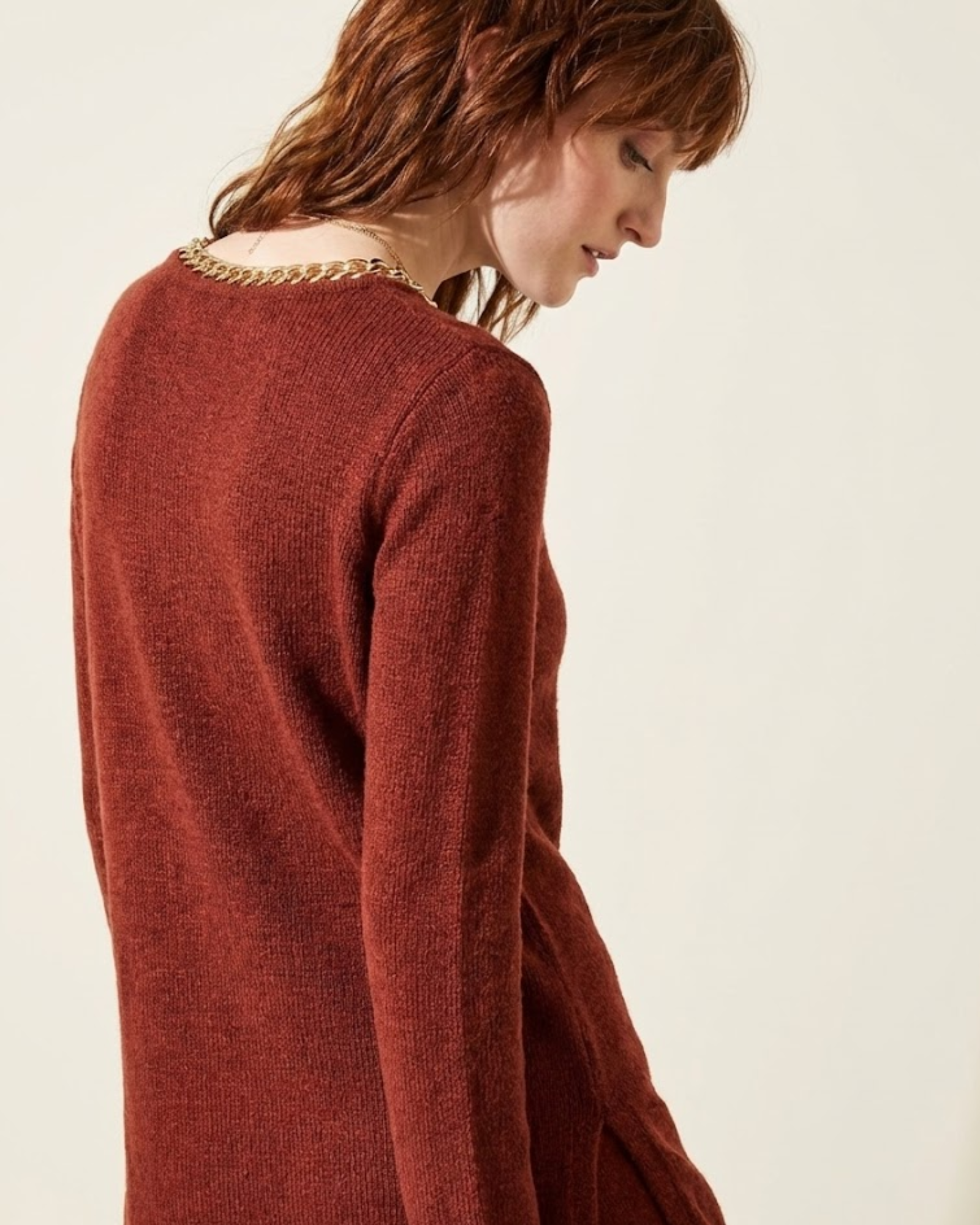Person wearing a rust-colored sweater against a plain background